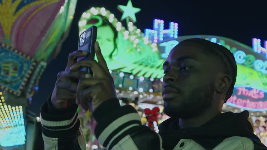 Close up of a young man using a phone to film on the amusement park at night
