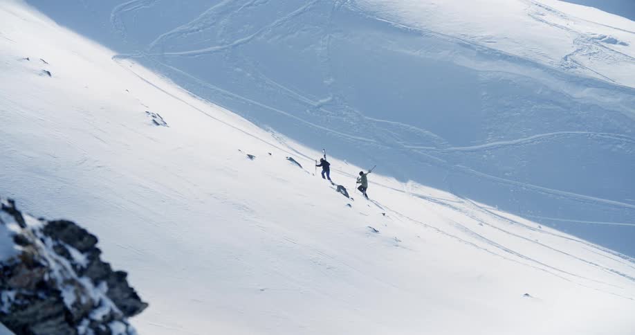 A pair of mountaineers ascend a snowy mountain slope during the day