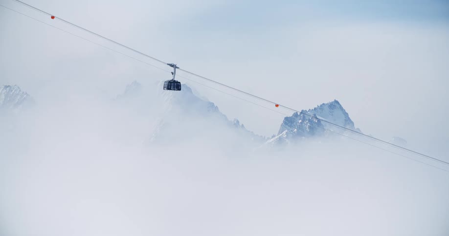 Wide view of ski lift descending mountain low visibility white out peak in background