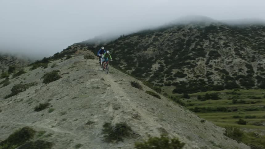 A pair of cyclists ride bicycle down a mountain slope during the day