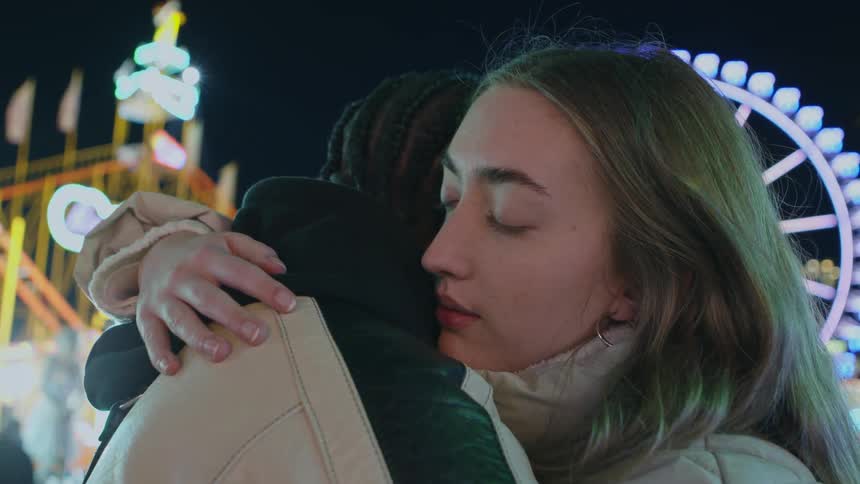 Couple hugs while standing in amusement park at night