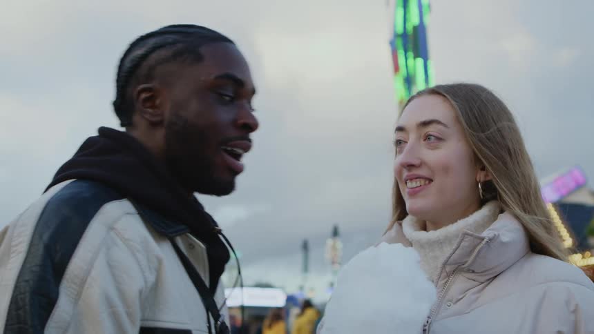 A man and woman chat while having cotton candy at a carnival