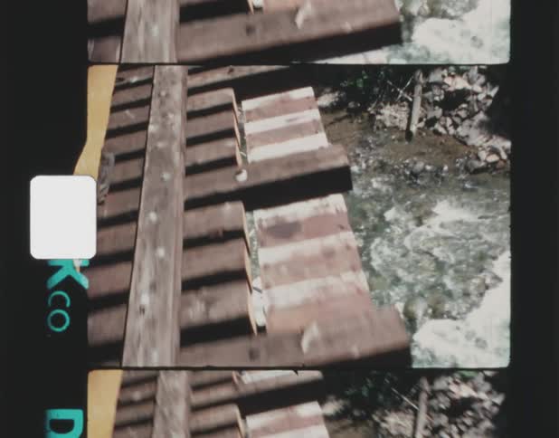 A train travels on the tracks above a rushing river via a tall bridge