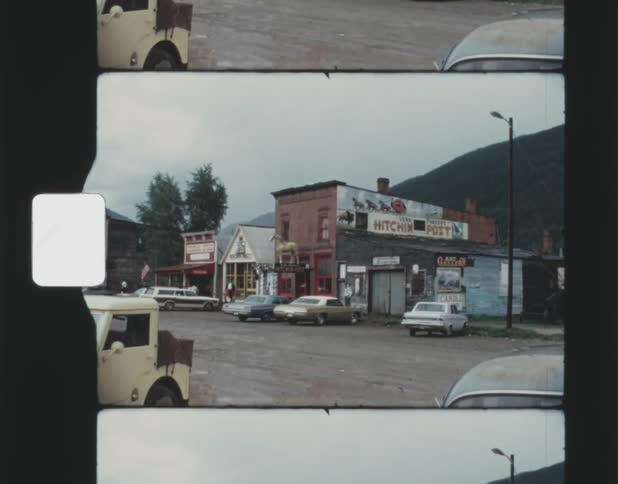 Pedestrians move along sidewalk in small town near stores at base of hills