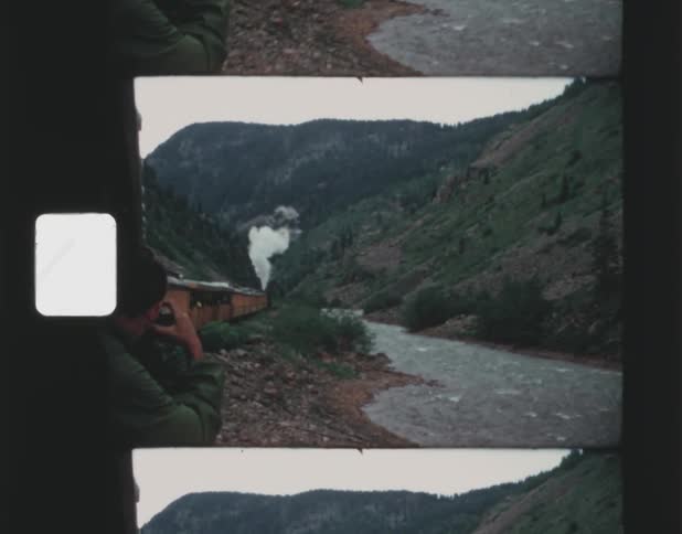 A man riding on a freight train takes a photo of the mountains