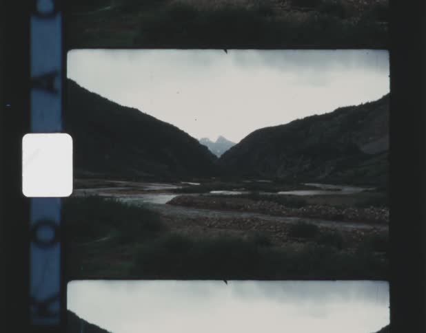 A vintage looking film shows some mountains with a sky behind them and grass in the front