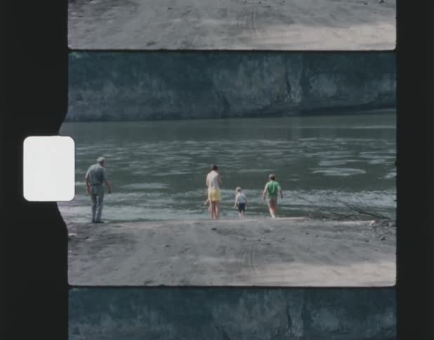 Old film footage of a family walking on the shore by a river