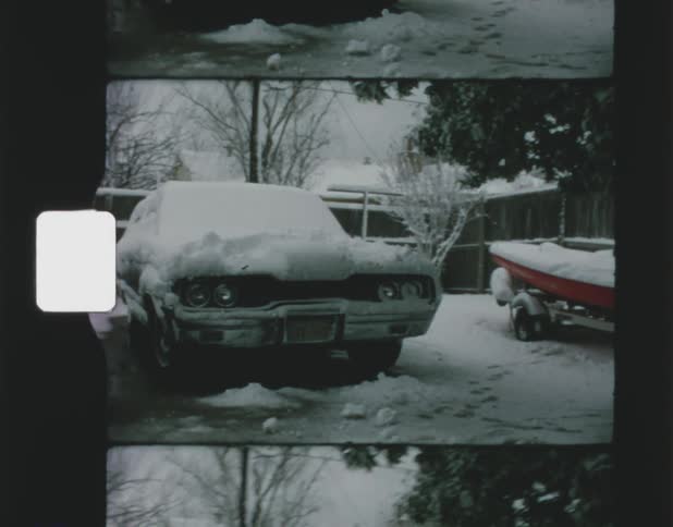 A pair of cars and a boat covered in snow parked next to a house on a winter day