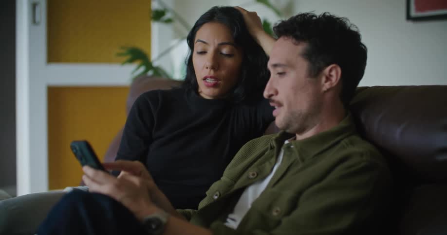 A man and woman look at a smartphone on the couch together