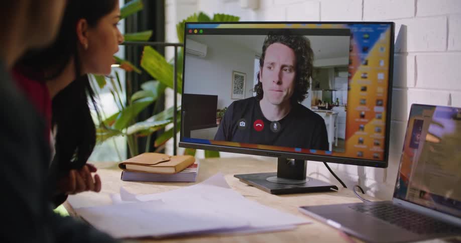 Two office workers are engaged in a video conference with another man and discussing a project