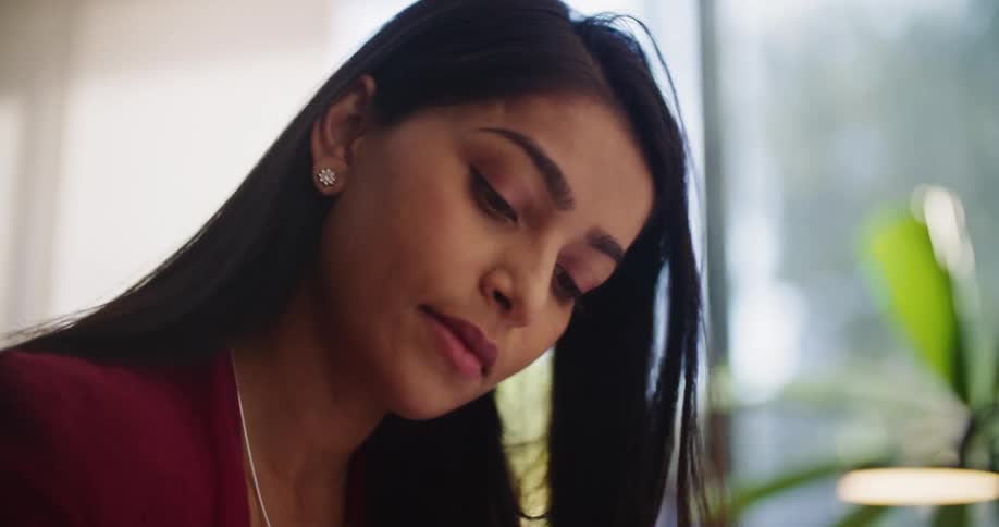 A woman is looking down as she writes and pauses for a moment to think