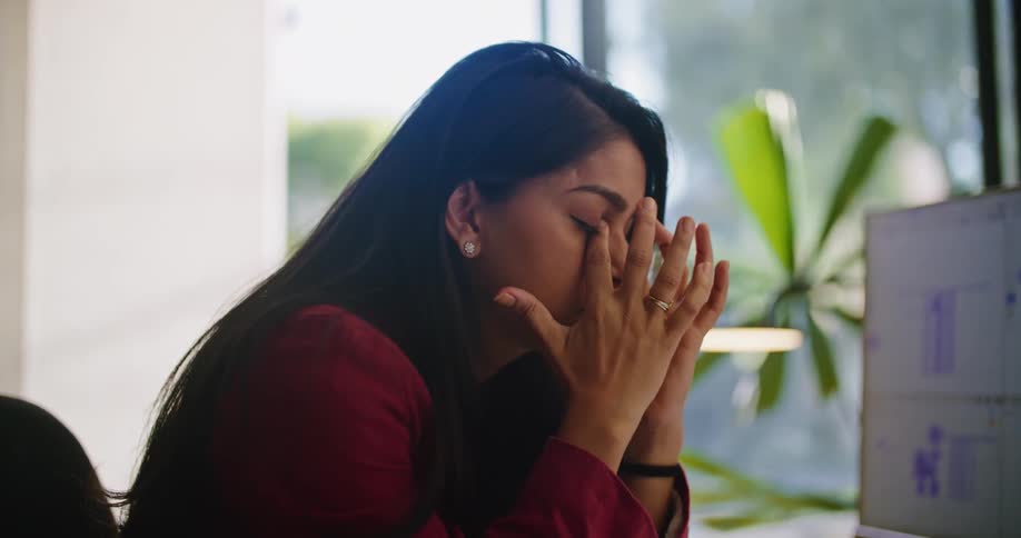 A woman sitting at her desk in front of a computer running her hands through her hair stressed