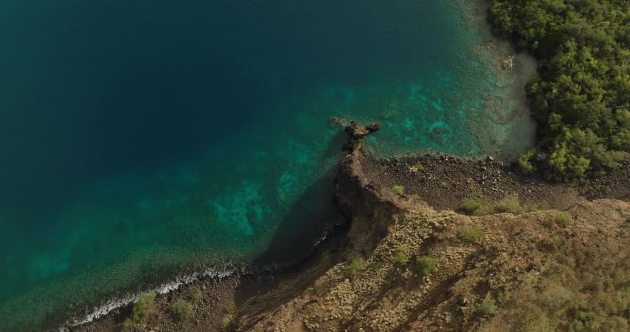 An aerial view of a rock formation that extends from a steep mountain cliff into the sea below