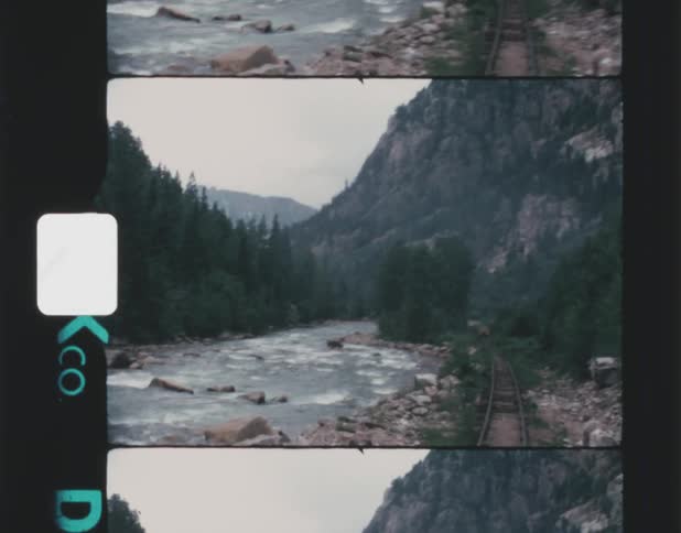 A river flowing at the bottom of a mountain while train tracks travel along the river