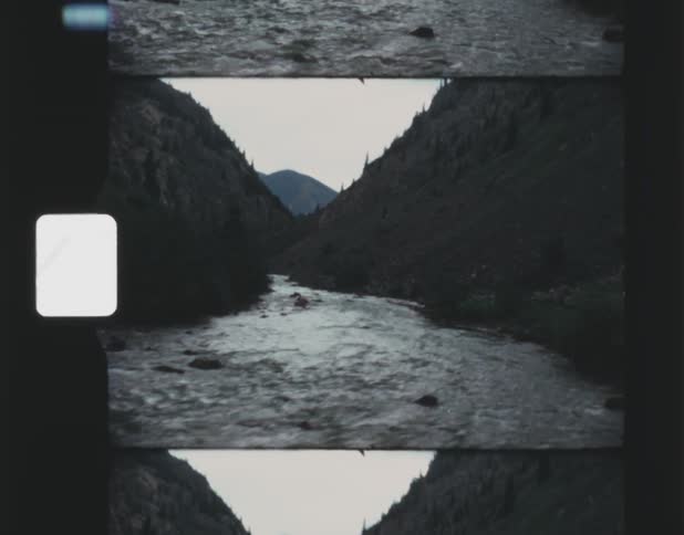 A stream runs between two mountains with rocks along the bank and a mountain in the distance