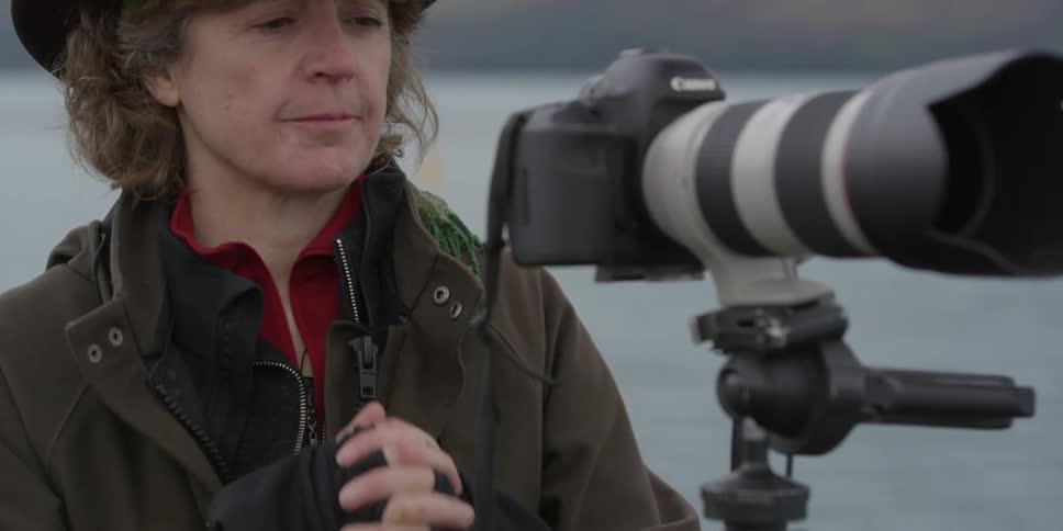 A female photographer rubs her hands together while standing in front of her camera