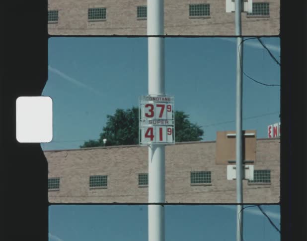A sign on a pole showing the price of gas and a building in the distance