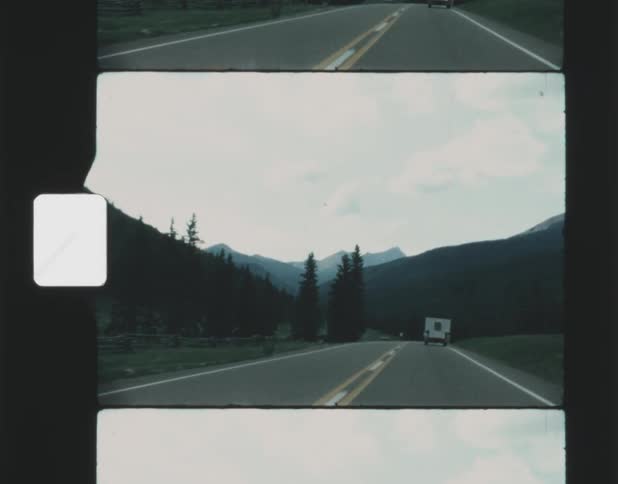 An old looking film features a person filming in a vehicle not shown and they are filming a recreational vehicle drive down the street