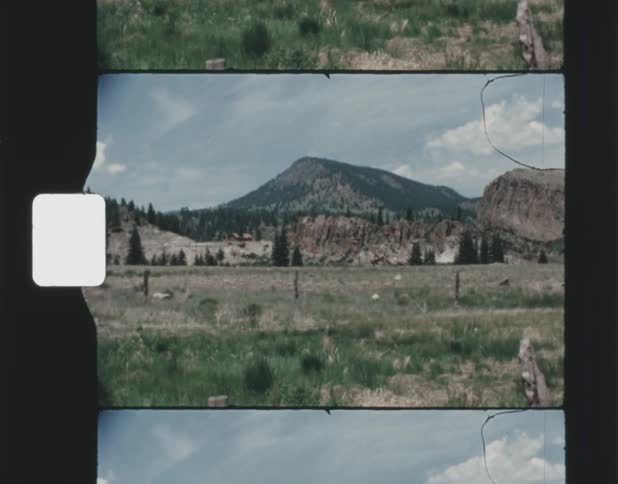 A tall mountain stands behind a wide open field and hills
