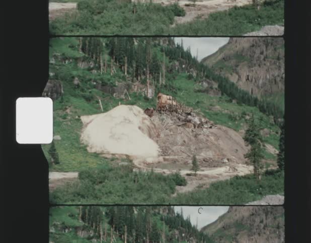 Vintage footage of a mound in the woods on a hillside with a cabin and some paths