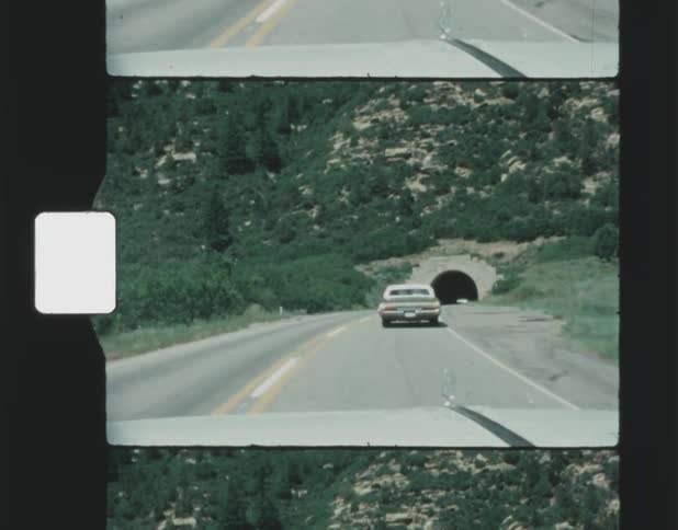 Old film footage of a car driving down a street about to enter a tunnel