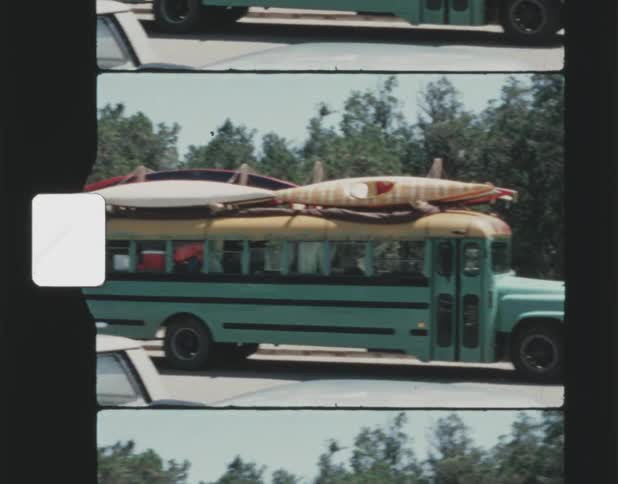 Vintage footage of a green school bus with several kayaks or surfboards strapped on with passengers onboard waiting to leave