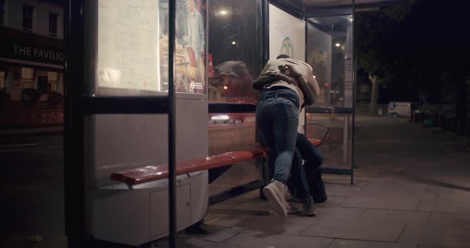 Two men sitting at a bus stop happily hug each other