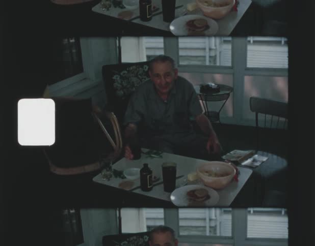 Man with shirt and pants sits at table holding a glass