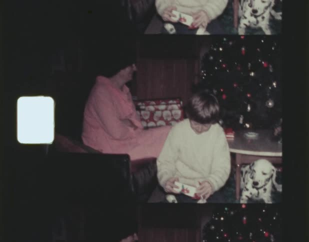 A mother watches her son open christmas presents with his dog