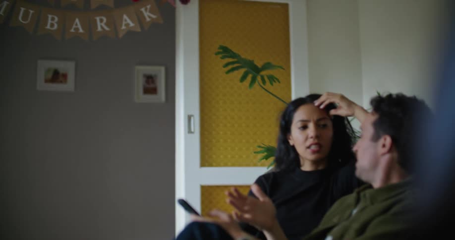 A man and woman sit on a couch indoors while having a conversation