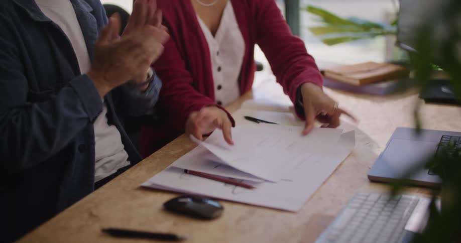 A man and woman sit at a desk in an office and look through papers as they talk