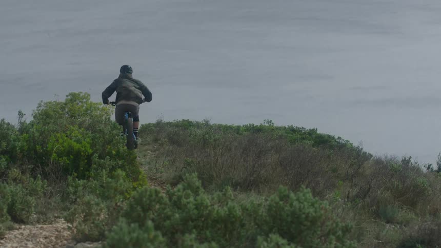A man rides his bicycle along a cliff overlooking the ocean
