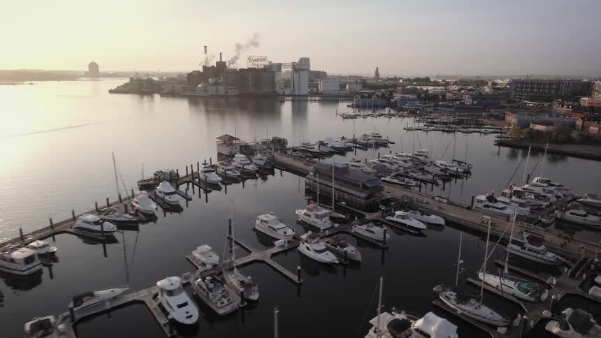 Dozens of boats are parked in a harbor near a factory