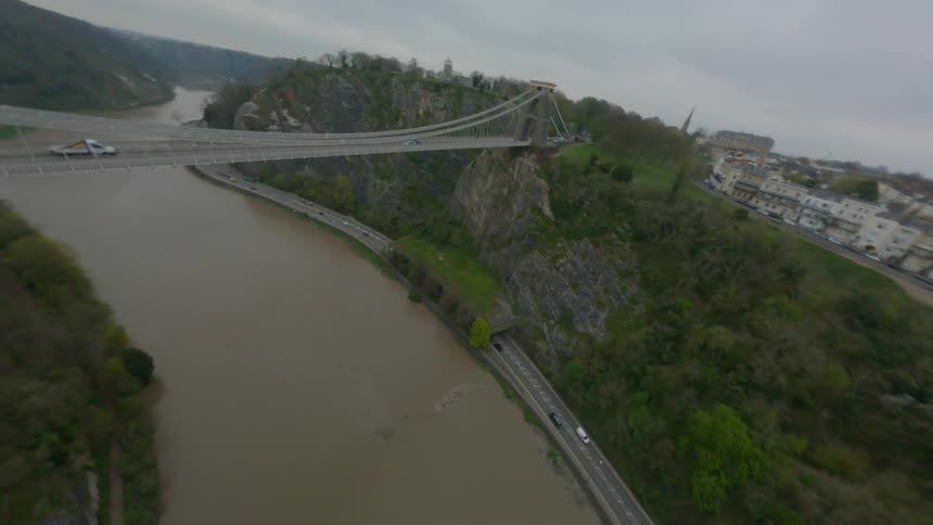 An aerial of a tall bridge over a large brown river and a road traveling next to the river