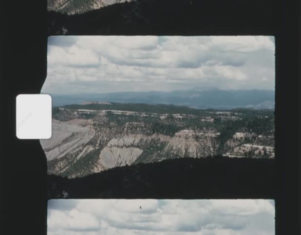 Forested mountains stand under a cloudy sky and there are mountains on the horizon