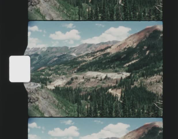 Road curves near top of mountain over forested valley and across from other mountains