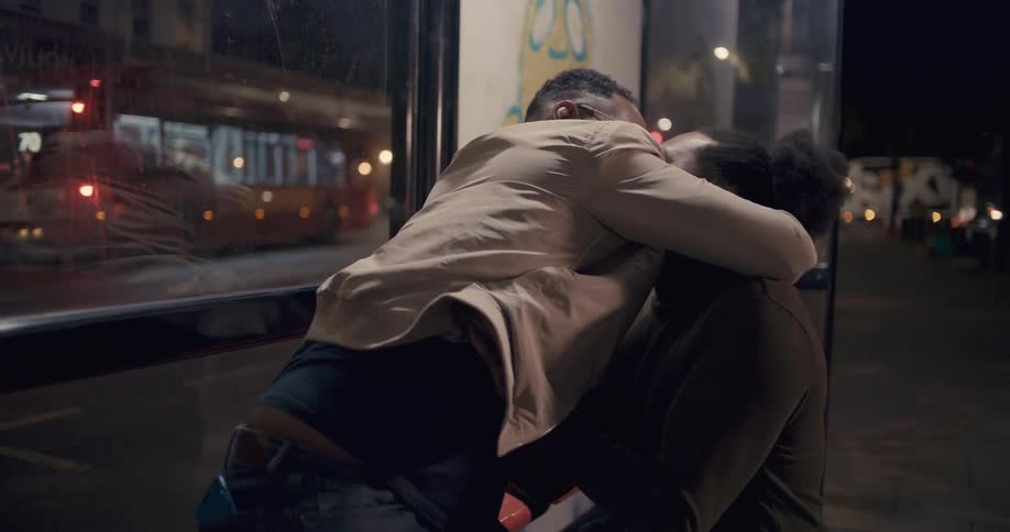 A man proposes to another man at a bus stop and offers an engagement ring on bended knee. They hug.