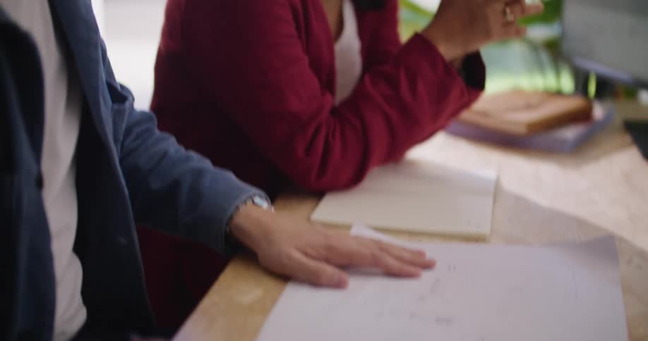 A man and woman sit at a desk while the man shows the woman a sketch he is working on and she talks with him about it