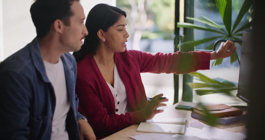 A woman points at a computer screen while talking to her male colleague