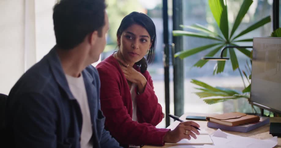 Businessman with mustache and blue shirt and businesswoman with red jacket sit at desk and work together at the office