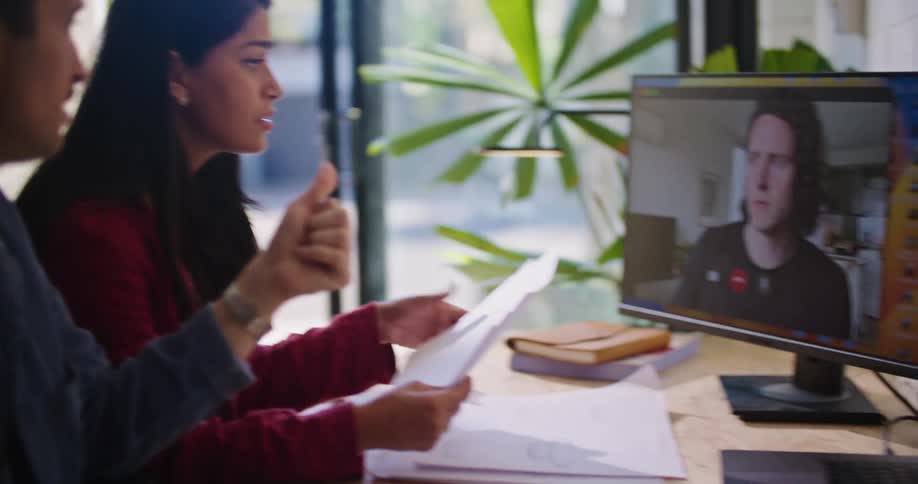 A work group is sitting at a desk and collaborating with another man via video conference