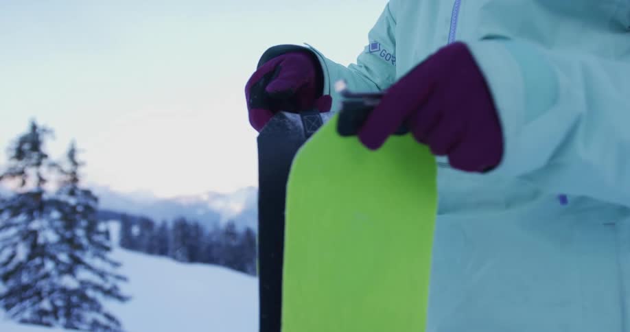 A close up of a person wearing gloves and a winter coat putting together a ski cover while they stand outdoors in the snow