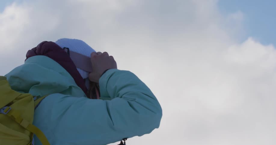 Woman with white hat light blue coat and yellow backpack wears goggles