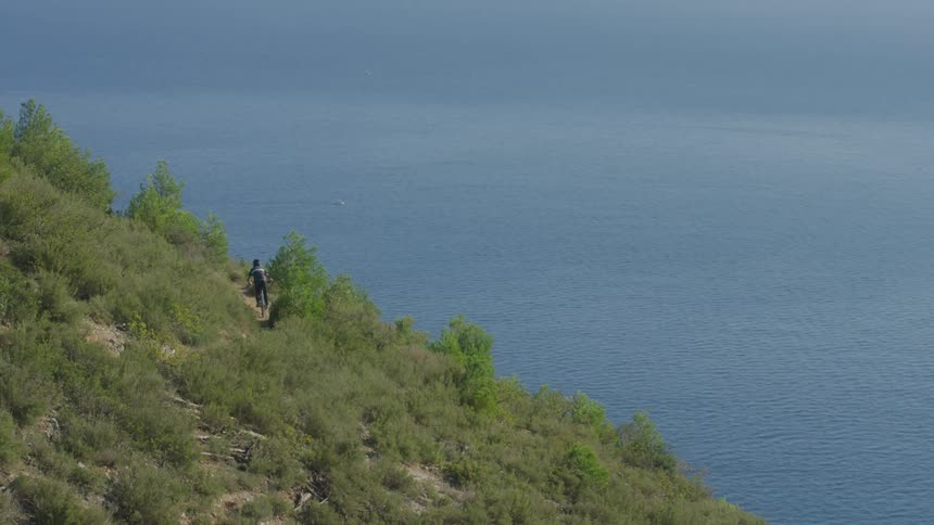 A cyclist rides down a green hill along the coastline