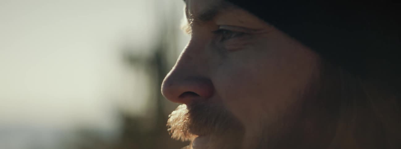 A man wears a beanie while standing in the woods and smiles
