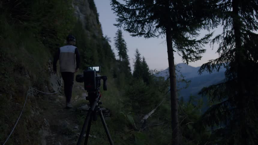 A male is setting up a camera in a wooded area