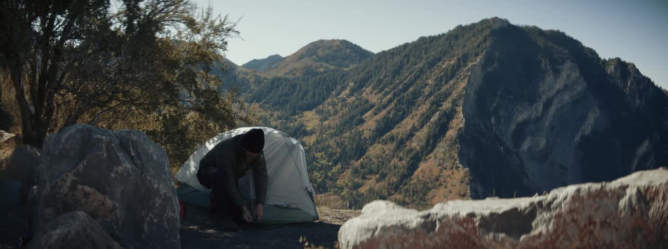 A man in a jacket sets up a tent while camping in a mountainous area