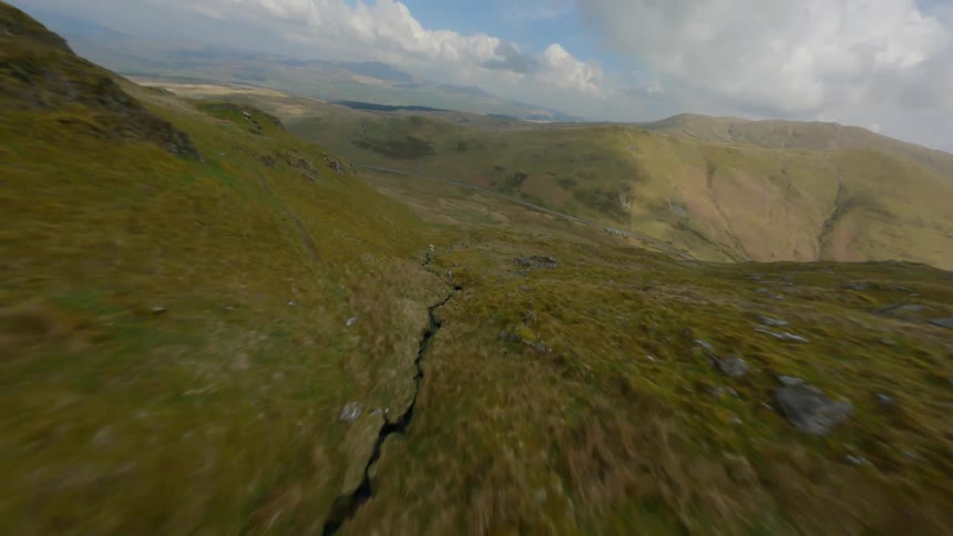 Drone footage traveling close to ground along crack or tiny creek in hilly mountainous landscape