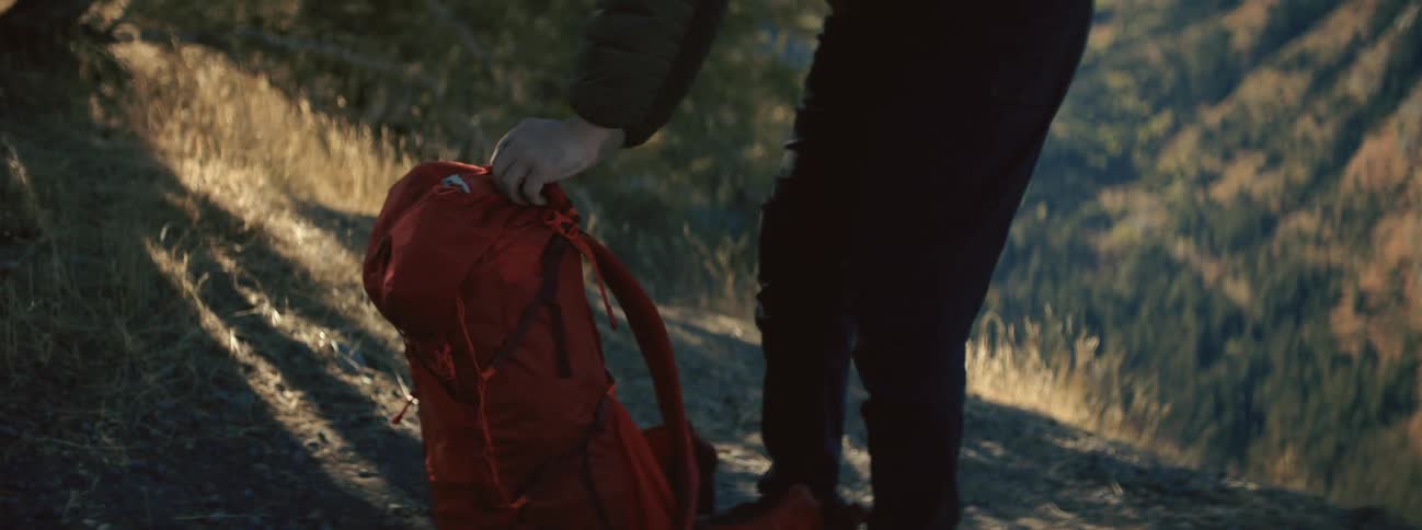 A man zips up his backpack while standing in a canyon