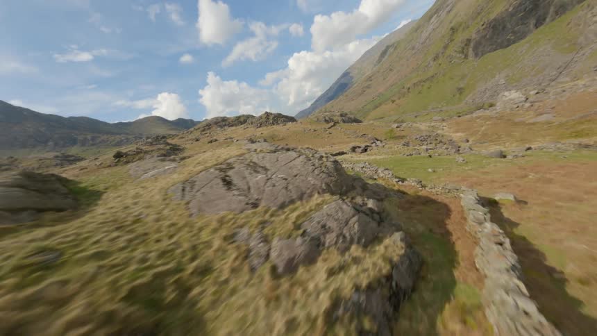Rock outcrops are scattered across the hillside with mountains in the distance and cumulus clouds in the sky